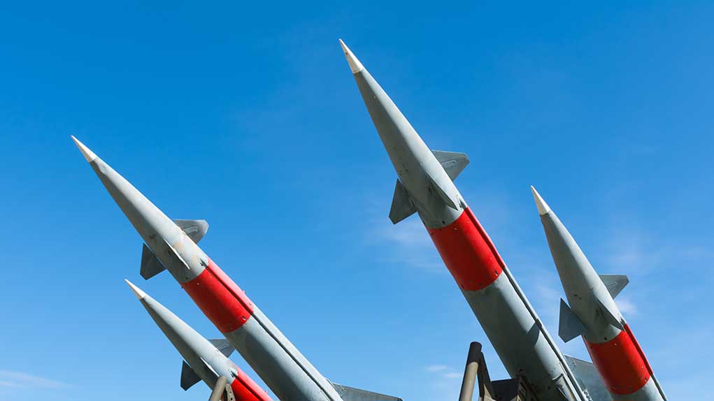 Four missiles pointing upwards under blue sky.
