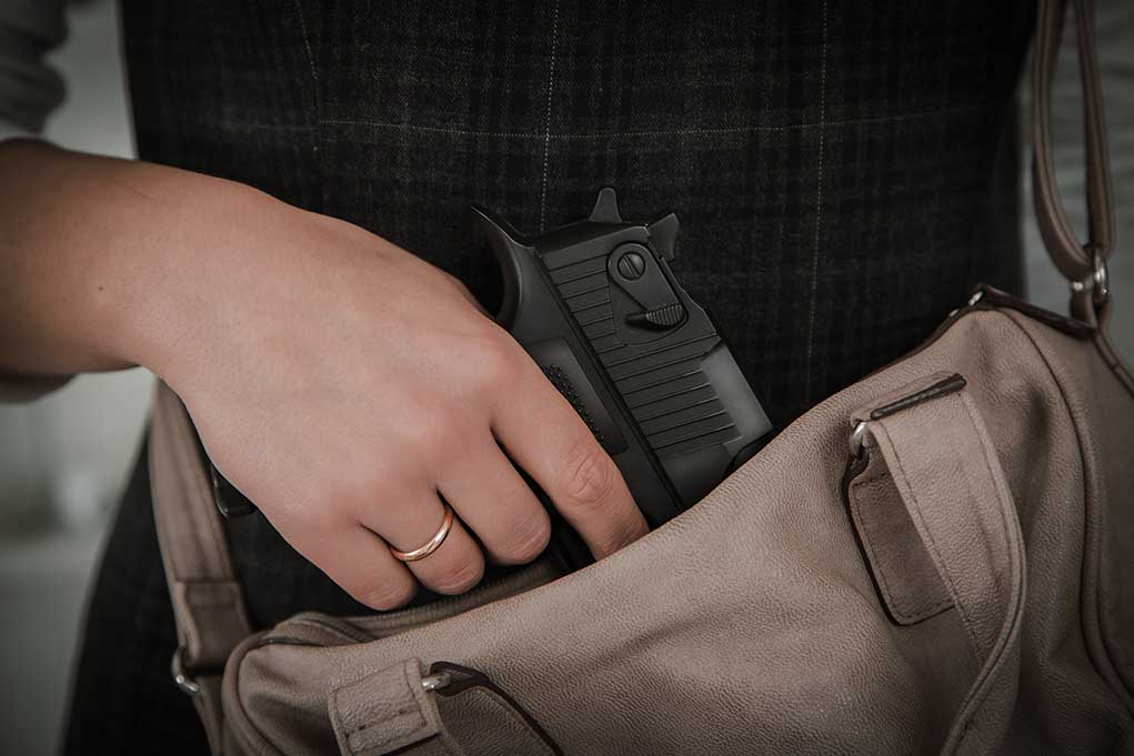 Hand placing handgun into beige handbag.