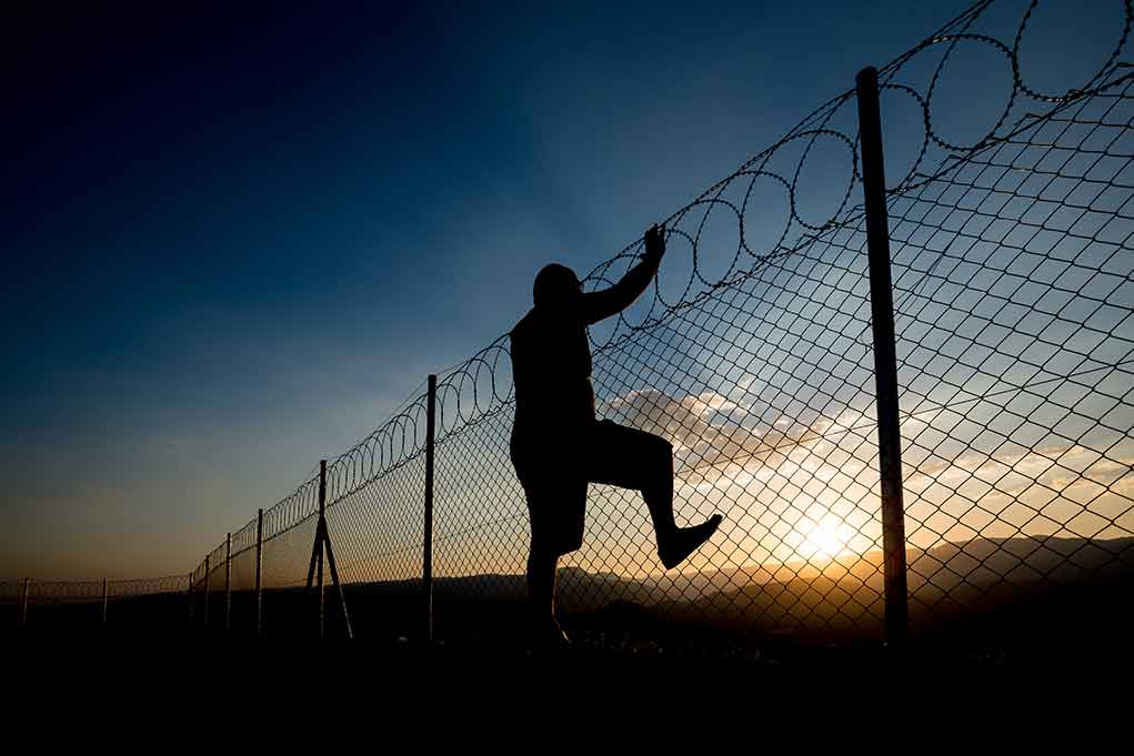 Silhouette of person climbing barbed wire fence at sunset