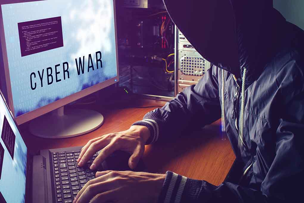 Hacker typing at desk with Cyber War screen