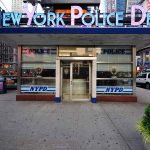 NYPD precinct building with signs on a city street