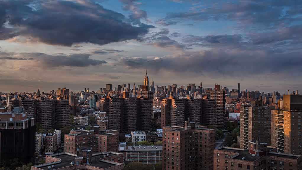 A panoramic view of New York City skyline during sunset with clouds