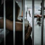 Cornhusker Clink Launches: Aggressive Immigration Stance Person sitting behind bars with arms wrapped around knees