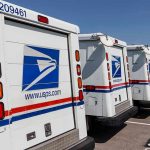 Key Nations HALT U.S. Postal Shipments – HEAVY DELAYS! Row of USPS mail trucks parked in lot.