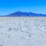 Tragic Crash: Racer’s Final Speed Quest Ends In Disaster A vast salt flat with a mountain range in the background under a clear blue sky