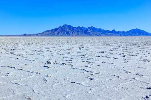 A vast salt flat with a mountain range in the background under a clear blue sky