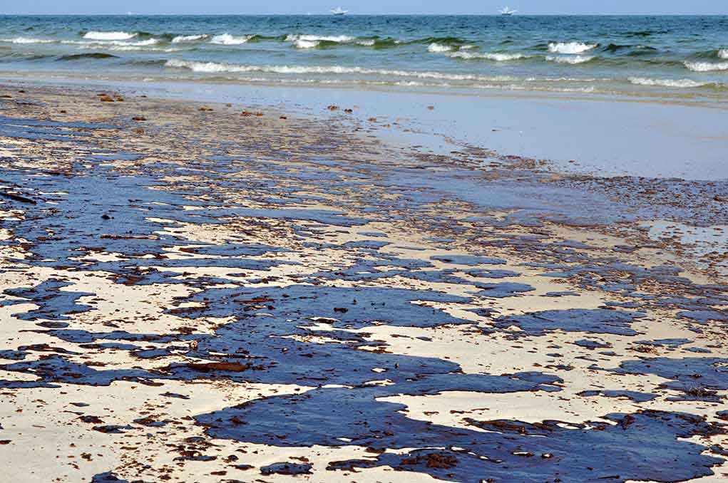 Oil spill on a sandy beach with waves in the background