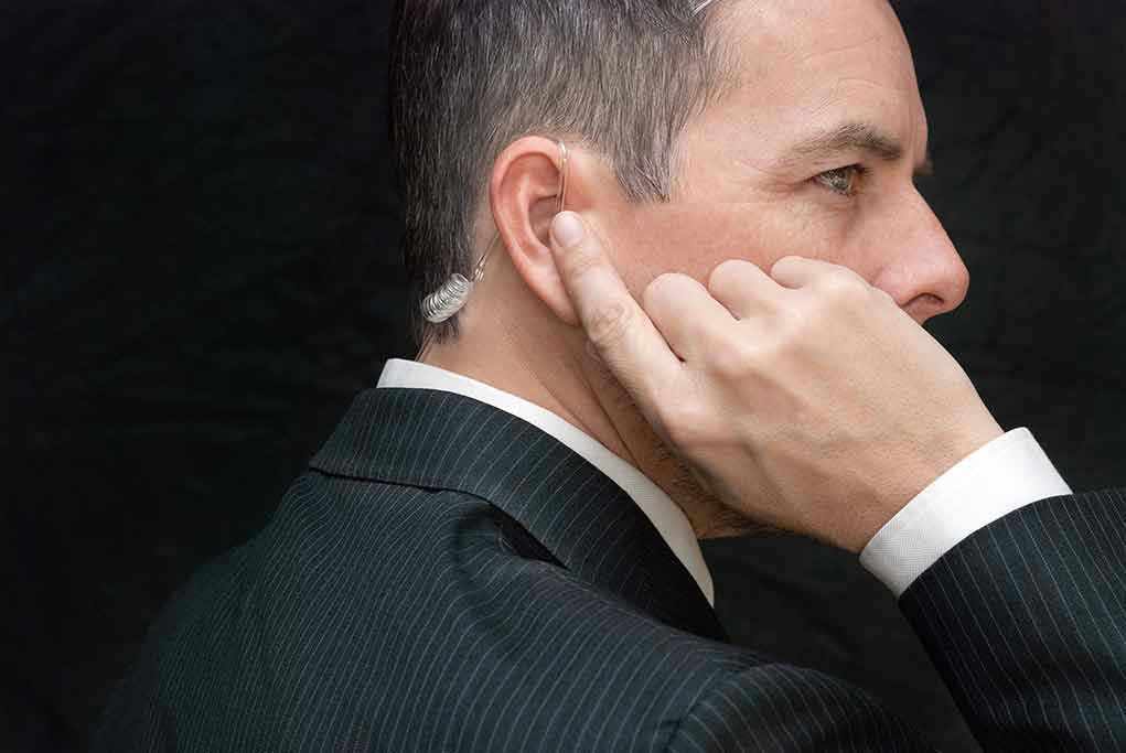 Man in suit adjusts earpiece with finger