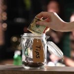 Hand placing dollar bill into a tip jar