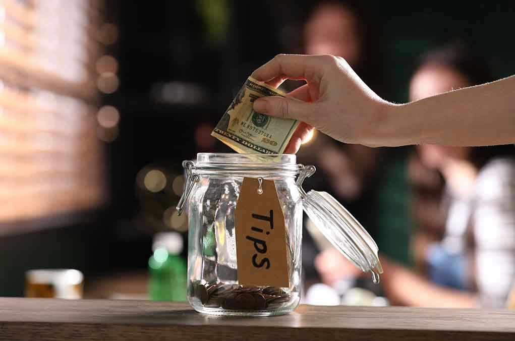 Hand placing dollar bill into a tip jar