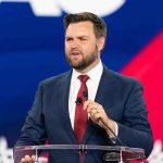 Vance’s Immigration Clash Stuns Campus Man speaking at a podium wearing suit and tie