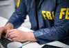 Person in FBI jacket typing on a laptop