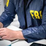 FBI Feud Explodes Over Kirk Assassination Person in FBI jacket typing on a laptop