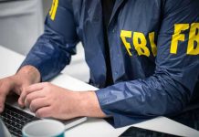 Person in FBI jacket typing on a laptop