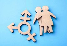 Trans Activist’s Appointment Ignites WOMEN’S RIGHTS FURY Wooden transgender symbol and couple figures on blue background.