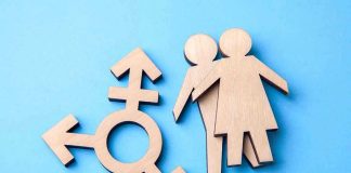 Trans Activist’s Appointment Ignites WOMEN’S RIGHTS FURY Wooden transgender symbol and couple figures on blue background.