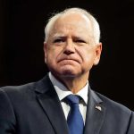 Walz Under Fire: Trump Slams Sanctuary Policies Man in suit with a U.S. flag pin.