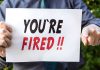 Fired and Rehired at LOWER Pay – Outrageous! Person holding YOURE FIRED sign.