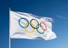 IOC ABANDONS Woke Transgender Policy – FINALLY! Olympic flag waving against clear blue sky.
