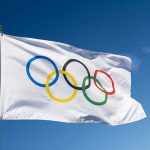 Olympic flag waving against clear blue sky.