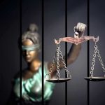 Blindfolded Lady Justice statue holding scales behind bars