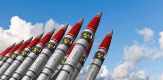 A row of military missiles with red tips and nuclear symbols against a blue sky