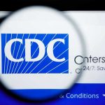 Newborns Lose Shield After Stunning CDC Reversal CDC logo magnified on a screen.