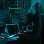 Adult Website Users EXPOSED! Hacker in dark room surrounded by computer screens.