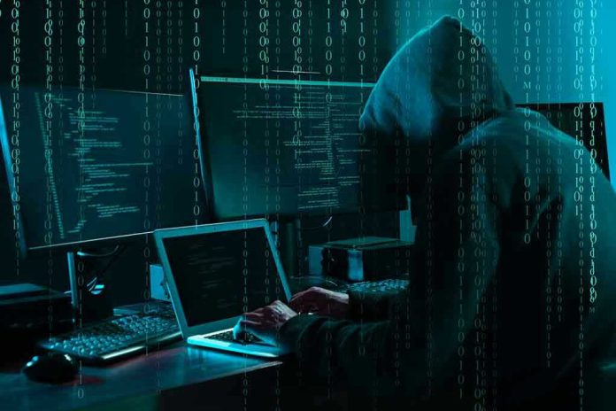 Hacker in dark room surrounded by computer screens.