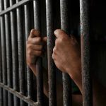 Judge Calls Out SCANDAL: 27-Year Innocent Imprisonment Hands gripping prison cell bars tightly.