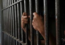 Judge Calls Out SCANDAL: 27-Year Innocent Imprisonment Hands gripping prison cell bars tightly.