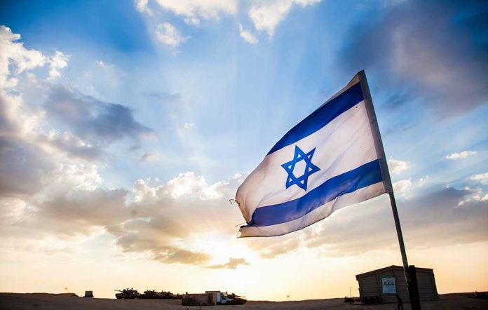 shutterstock_154973519.jpg Israeli flag waving against a sunset backdrop with clouds