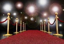 A red carpet lined with gold stanchions and ropes under bright spotlights