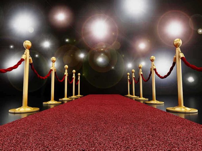 A red carpet lined with gold stanchions and ropes under bright spotlights