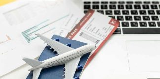 A model airplane on a blue passport next to a laptop and boarding pass