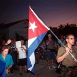 A group of people participating in a protest march holding a Cuban flag