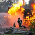 Wildfire Payouts SHATTER Records Firefighter battling a large fire with water spray