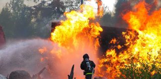 Wildfire Payouts SHATTER Records Firefighter battling a large fire with water spray