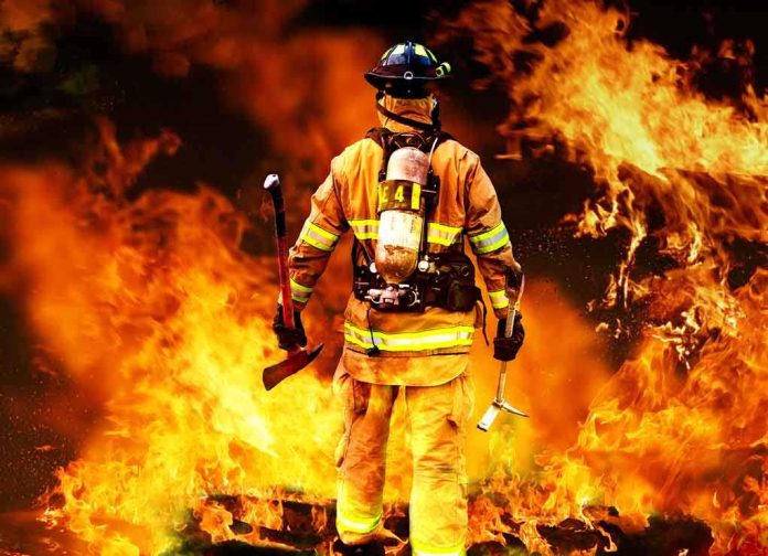 shutterstock_80081197-1 Firefighter standing in front of a large fire, equipped with tools