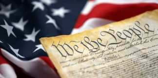 Schools Clash Over ‘Teaching America’ Close-up of a historical document with the American flag in the background