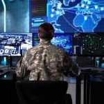 Military personnel monitoring multiple screens in a command center