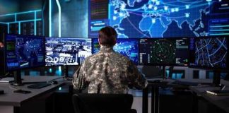 Military personnel monitoring multiple screens in a command center