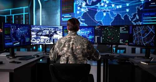 Military personnel monitoring multiple screens in a command center