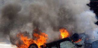 Trunk Turns Bomb on Quiet Jersey Street An overturned car engulfed in flames and smoke on a city street