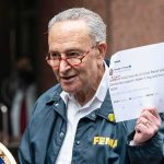 Heckler Torches Schumer’s Anti-Corruption Rollout man in FEMA jacket holding a printed tweet