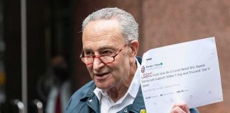 Heckler Torches Schumer’s Anti-Corruption Rollout man in FEMA jacket holding a printed tweet