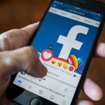 Hand using smartphone with Facebook reactions on screen