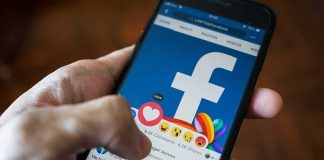 Hand using smartphone with Facebook reactions on screen