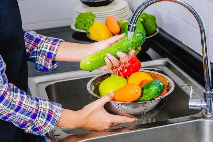 Hands washing cucumbers and bell peppers under a kitchen faucet