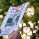 Abduction Mystery Lingers — FBI Cash on the Table Hands holding a missing person flyer outdoors